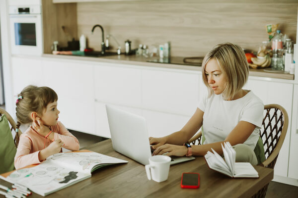 blonde mom working at home on the computer while watching her daughter