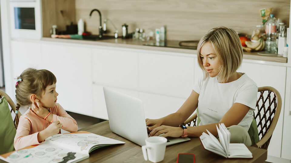 blonde mom working at home on the computer while watching her daughter